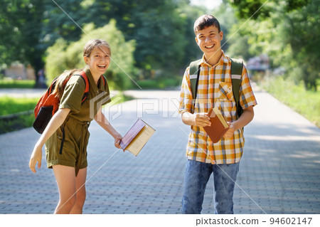 portrait of students in a city park, teenage schoolchildren a boy and a girl are standing on the path and discussing lessons, reading a book and talking 94602147