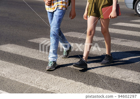teenage schoolchildren, a boy and a girl cross the road at a pedestrian crossing teenage schoolchildren, a boy and a girl cross the road at a pedestrian crossing 94602297