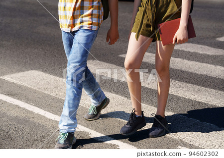teenage schoolchildren, a boy and a girl cross the road at a pedestrian crossing 94602302