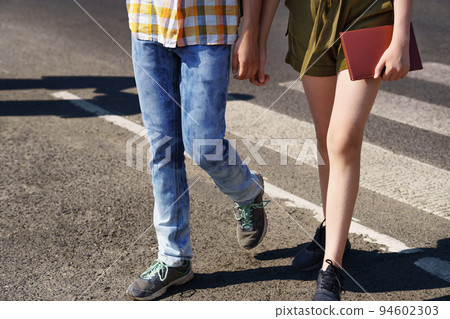 teenage schoolchildren, a boy and a girl cross the road at a pedestrian crossing 94602303