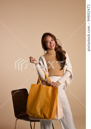 Attractive young woman carrying shopping bags standing on beige background. Black Friday, sale, shopping concept 94602471
