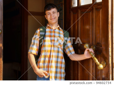 a teenage boy, being a student, stands at the entrance door to the school buildings a teenage boy, being a student, stands at the entrance door to the school buildings 94602734