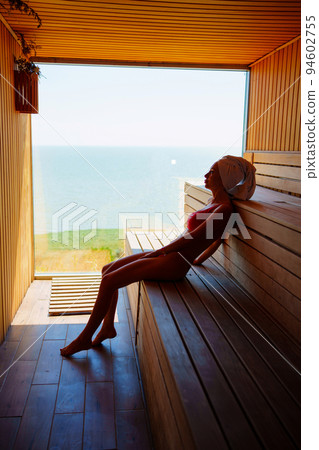 woman in a red swimsuit sits on a bench in the sauna with the panoramic window. woman in a red swimsuit sits on a bench in the sauna with the panoramic window. 94602755