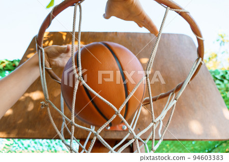 close view of hands throwing a ball into a basketball basket, teenage boy playing at home in the backyard, outdoor activities on summer vacation 94603383