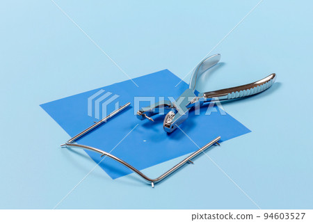 Dental hole punch, metal frame and rubber dam on blue. Dental hole punch, metal frame and rubber dam on blue. 94603527