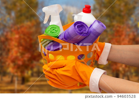 Woman's hands in protective glove with garbage bags, bottles of glass cleaner in orange basket on beige background. Woman's hands in protective glove with garbage bags, bottles of glass cleaner in orange basket on beige background. 94603528