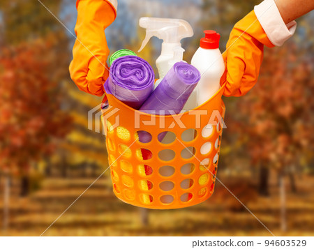 Woman's hands in protective glove with garbage bags, bottles of glass cleaner in orange basket. Woman's hands in protective glove with garbage bags, bottles of glass cleaner in orange basket. 94603529