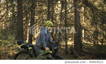 The woman travel on mixed terrain cycle touring with bike bikepacking. The traveler journey with bicycle bags. Magic forest park. 94603612
