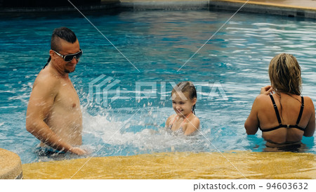 The mother and father with little daughter have fun in the pool. Mom and dad plays with the child. The family enjoy summer vacation in a swimming. The mother and father with little daughter have fun in the pool. Mom and dad plays with the child. The family enjoy summer vacation in a swimming. 94603632