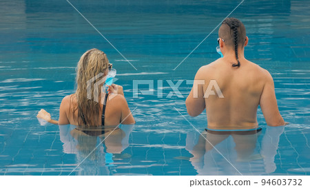 The loving couple hugs and kisses, drinking blue cocktail alcohol liquor in swimming pool at hotel outdoor. Portrait of caucasian man and woman. 94603732