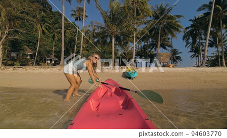 Woman pulls canoe with paddle to azure sea water from beach Woman pulls canoe with paddle to azure sea water from beach 94603770