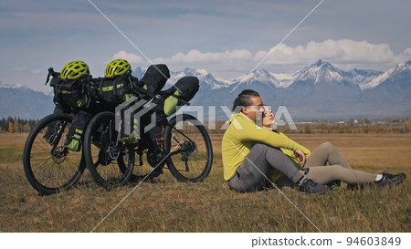 The man and woman travel on mixed terrain cycle touring with bikepacking. The two people journey with bicycle bags. Mountain snow capped. The man and woman travel on mixed terrain cycle touring with bikepacking. The two people journey with bicycle bags. Mountain snow capped. 94603849