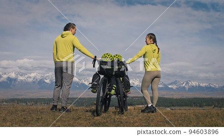 The man and woman travel on mixed terrain cycle touring with bikepacking. The love couple journey with tent in with bicycle bags. Stylish sportswear. The man and woman travel on mixed terrain cycle touring with bikepacking. The love couple journey with tent in with bicycle bags. Stylish sportswear. 94603896
