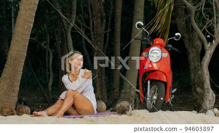 Scooter road trip. Woman alone on red motorbike in white clothes on sand beach by ocean. One girl caucasian tourist walk near tropical palm tree. Scooter road trip. Woman alone on red motorbike in white clothes on sand beach by ocean. One girl caucasian tourist walk near tropical palm tree. 94603897
