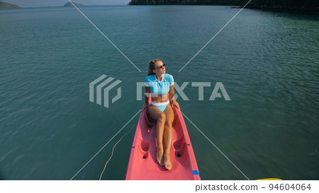 Pretty slim woman in elegant swimsuit lies in pink plastic kayak drifting on azure ocean at exotic resort upper view. 94604064