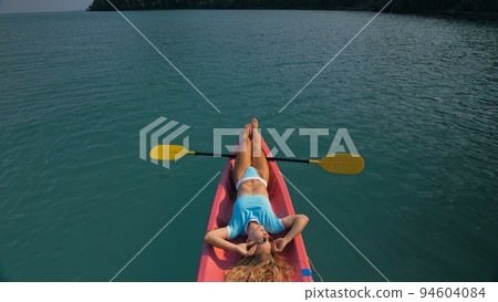Pretty slim woman in elegant swimsuit lies in pink plastic kayak drifting on azure ocean at exotic resort upper view. Pretty slim woman in elegant swimsuit lies in pink plastic kayak drifting on azure ocean at exotic resort upper view. 94604084