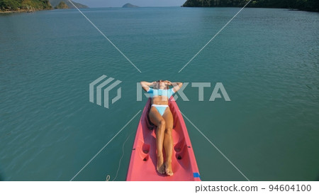 Pretty slim woman in elegant swimsuit lies in pink plastic kayak drifting on azure ocean at exotic resort upper view. 94604100