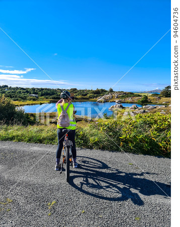 Lady with bicycle taking smartphone photos of a lake by Burtonport, County Donegal, Ireland - Seen from the Railway walk 94604736
