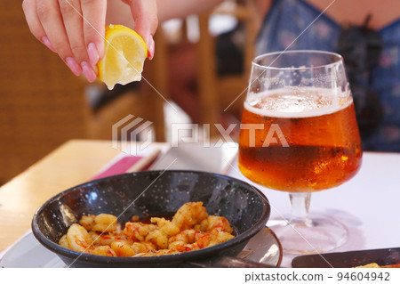 fried shrimps with lemon slice, garlic sauce aioli and tomato ketchup frying pan close up photo with beer 94604942