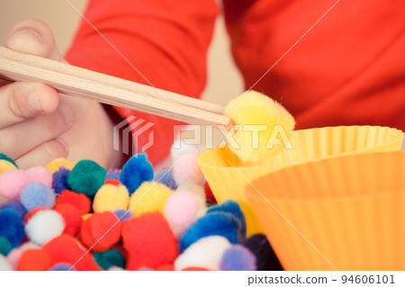 Preschooler playing with pompoms, wooden tongs and cups. Development of kids motor skills Preschooler playing with pompoms, wooden tongs and cups. Development of kids motor skills 94606101