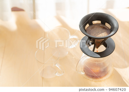 [Japan] Coarsely ground coffee beans in a coffee server, glass and dripper placed on the floor by the window where the morning sun shines 94607420