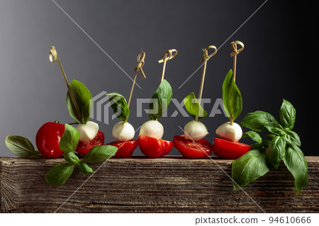 Mozzarella with basil and tomatoes on an old wooden board. 94610666