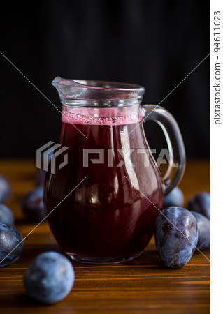 plum syrup in a glass decanter on a wooden table 94611023