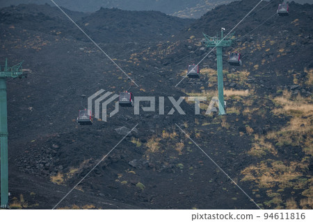 High angle view of cable cars moving over volcanic landscape. Mode of transport at famous Mount Etna. Scenic view of erupted crater with ash at popular tourist attraction. 94611816