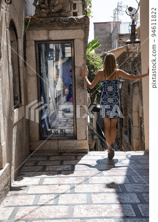 Taormina, Sicily, Italy. August 26, 2022. Female tourists standing by glass window outside shop. Rear view of woman exploring alley amidst old buildings in town during summer vacation. 94611822