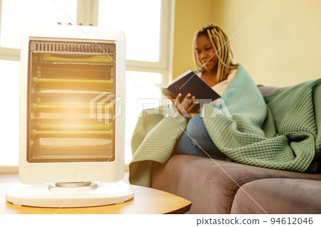 latin american woman with blanket reading a book in cold room with heater latin american woman with blanket reading a book in cold room with heater 94612046