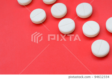 A few white tablets lie on a bright red background surface. Background image on medical and pharmaceutical topics A few white tablets lie on a bright red background surface. Background image on medical and pharmaceutical topics 94612334