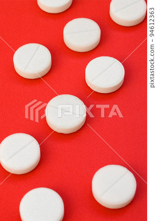 A few white tablets lie on a bright red background surface. Background image on medical and pharmaceutical topics 94612363