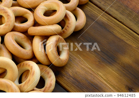 A lot of fresh yellow bagels lie on the surface of the old dark wood. A popular kind of flour products. One of the traditional Russian treats for tea 94612485