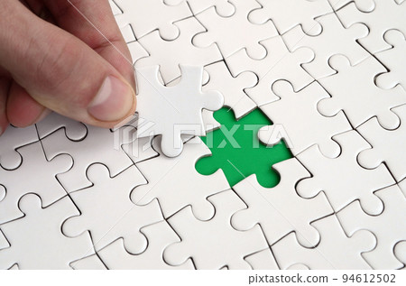 The human hand fills the last missing elements of the surface from the jigsaw puzzle. The concept of the completion of the initiated cases The human hand fills the last missing elements of the surface from the jigsaw puzzle. The concept of the completion of the initiated cases 94612502