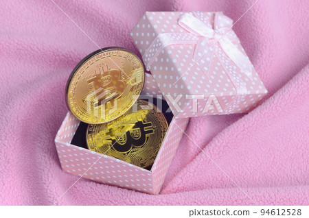The golden bitcoin lies in a small pink gift box with a small bow on a blanket made of soft and fluffy light pink fleece fabric with a large number of relief folds The golden bitcoin lies in a small pink gift box with a small bow on a blanket made of soft and fluffy light pink fleece fabric with a large number of relief folds 94612528