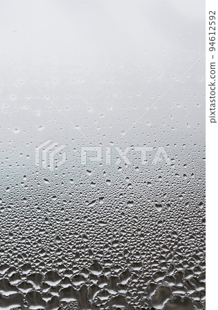 A photo of the glass surface of the window, covered with a multitude of droplets of various sizes. Background texture of a dense layer of condensate on glass A photo of the glass surface of the window, covered with a multitude of droplets of various sizes. Background texture of a dense layer of condensate on glass 94612592