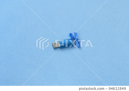 Brilliant blue usb flash memory card with a blue bow lies on a blanket of soft and furry light blue fleece fabric. Classic female gift design for a memory card 94612849