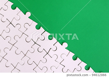Fragment of a folded white jigsaw puzzle on the background of a green plastic surface. Texture photo with copy space for text Fragment of a folded white jigsaw puzzle on the background of a green plastic surface. Texture photo with copy space for text 94612866