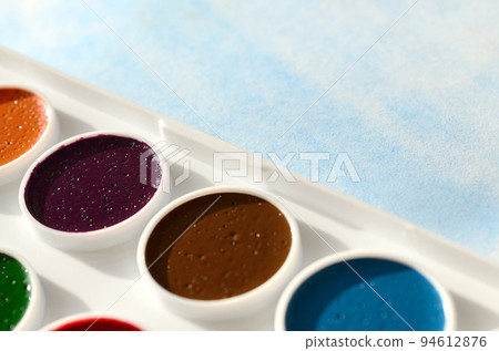 A new set of watercolors lies on a sheet of paper, which shows an abstract watercolor drawing in the form of blue strokes. The concept of amateur painting among teenagers 94612876