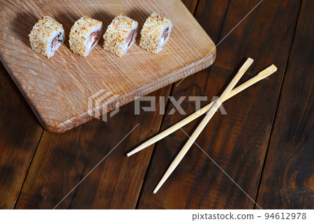A detailed shot of a set of Japanese sushi rolls and a device for their use chopsticks , which are located on a wooden cutting board on a table in the kitchen of a sushi bar A detailed shot of a set of Japanese sushi rolls and a device for their use chopsticks , which are located on a wooden cutting board on a table in the kitchen of a sushi bar 94612978