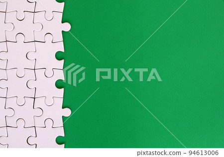 Fragment of a folded white jigsaw puzzle on the background of a green plastic surface. Texture photo with copy space for text 94613006