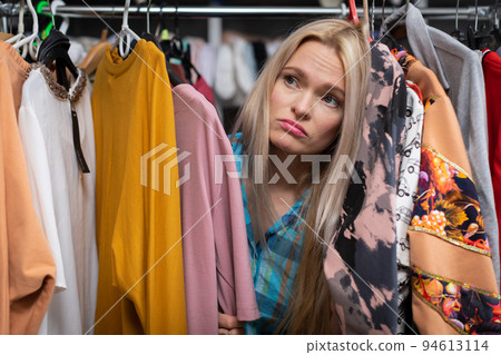 A sad blonde woman shopping in a clothing store. A sad blonde woman shopping in a clothing store. 94613114
