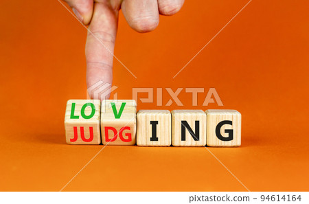 Loving or judging symbol. Concept words Loving or Judging on wooden cubes. Businessman hand. Beautiful orange table orange background. Business loving or judging concept. Copy space. Loving or judging symbol. Concept words Loving or Judging on wooden cubes. Businessman hand. Beautiful orange table orange background. Business loving or judging concept. Copy space. 94614164