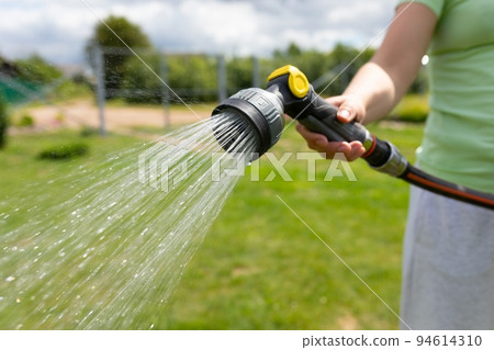 woman watering the lawn with a garden hose with a watering can woman watering the lawn with a garden hose with a watering can 94614310