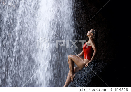 Woman sit on rock under waterfall in tropical jungle 94614808
