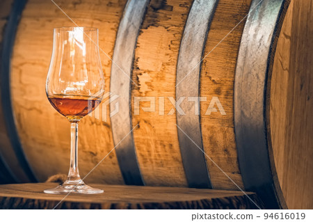 Close up of white port wine in wineglass in front of oak barrel Close up of white port wine in wineglass in front of oak barrel 94616019