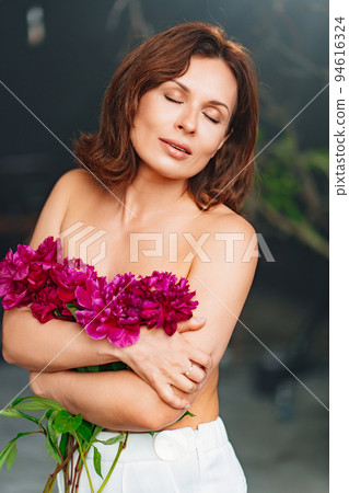 a gentle woman with closed eyes and bare shoulders and arms with a peonies. a gentle woman with closed eyes and bare shoulders and arms with a peonies. 94616324