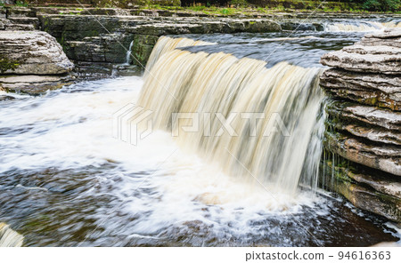 Aysgarth Falls are a three levels one mile stretch waterfalls in Yorkshire Dales National Park, River Ure, Northern England. Long exposure effect photo, selective focus on stones Aysgarth Falls are a three levels one mile stretch waterfalls in Yorkshire Dales National Park, River Ure, Northern England. Long exposure effect photo, selective focus on stones 94616363