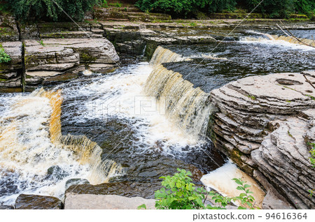 Aysgarth Falls are a three levels one mile stretch waterfalls in Yorkshire Dales National Park, River Ure, Northern England. Long exposure effect photo, selective focus on stones Aysgarth Falls are a three levels one mile stretch waterfalls in Yorkshire Dales National Park, River Ure, Northern England. Long exposure effect photo, selective focus on stones 94616364