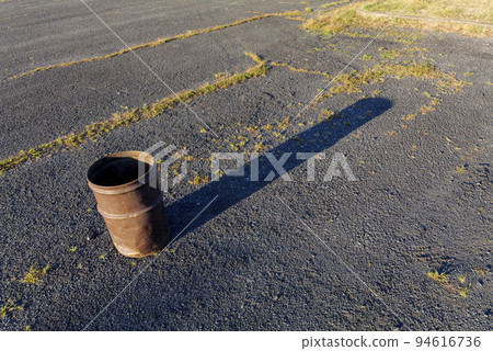 Garbage can in a metal barrel outside on asphalt at the parking lot. 94616736